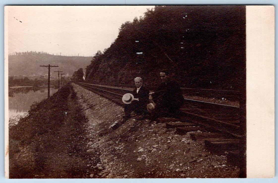 RPPC 2 MEN SITTING ON RAILROAD TRAIN TRACKS*HATS IN HAND*ARISTA STAMP BOX