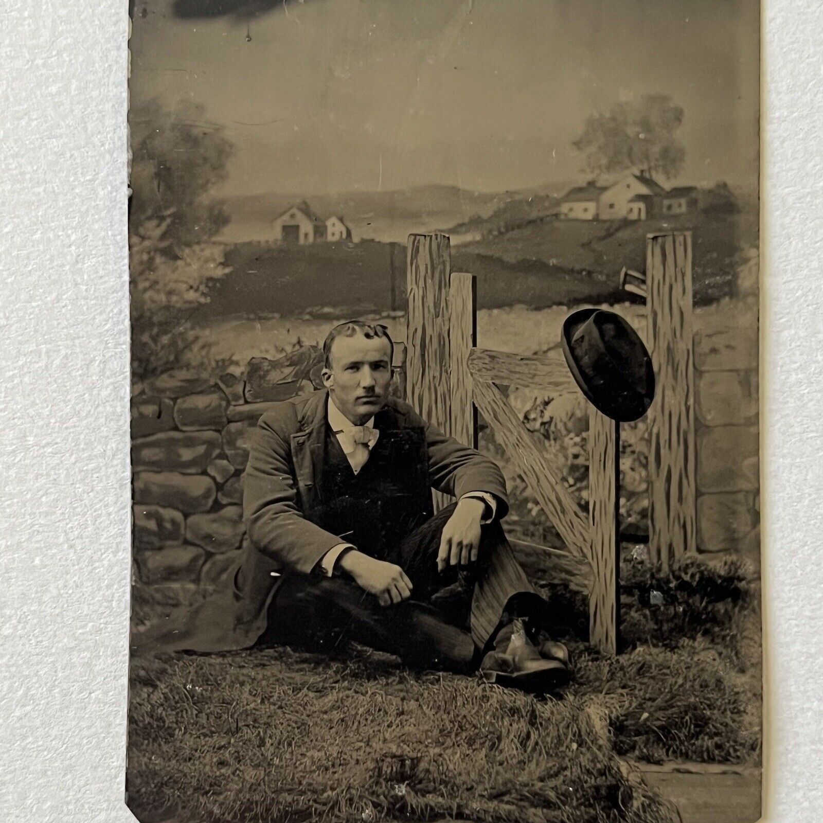 Antique Tintype Photograph Handsome Young Man Sitting On Ground Prop Fence Hat