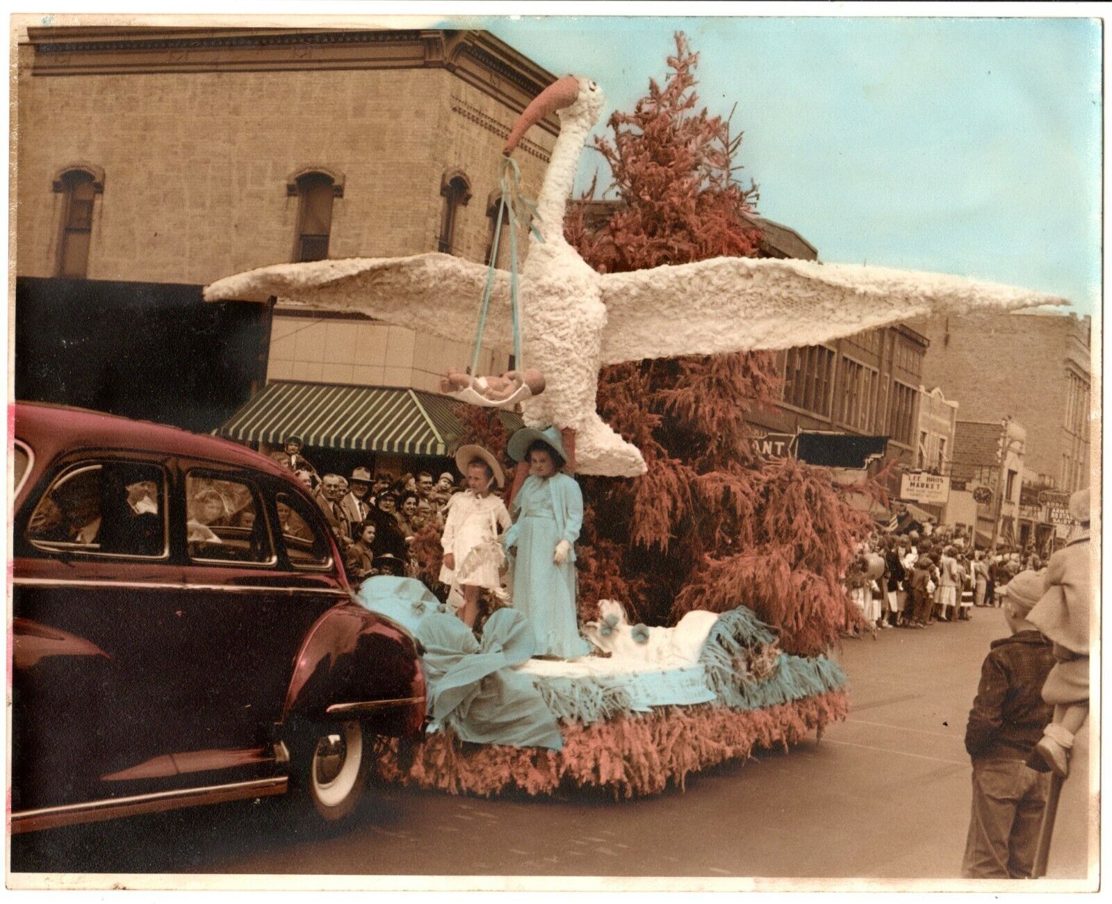 Great 1940\'s tinted image,parade, float,huge stork,baby in sling,Baby Boomers