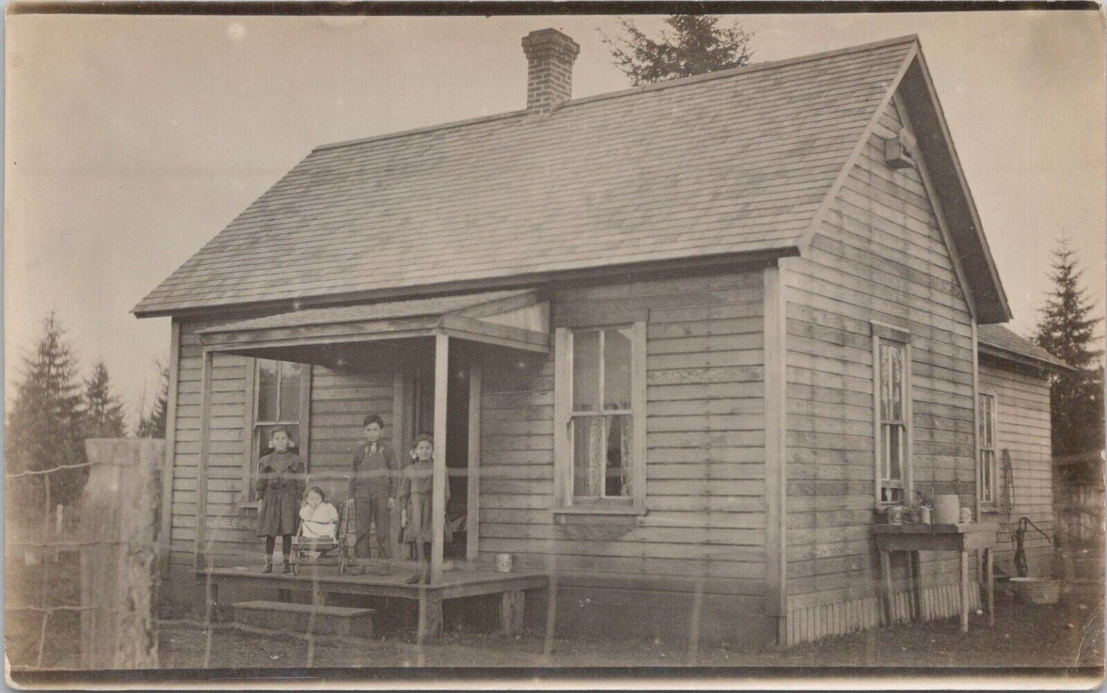 RPPC Poverty Scene Four Children Posing on Small Wooden House Porch early 1900s