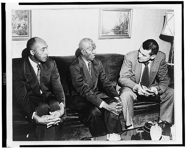 Two unidentified African American men seated on a sofa, talking to a young ma...