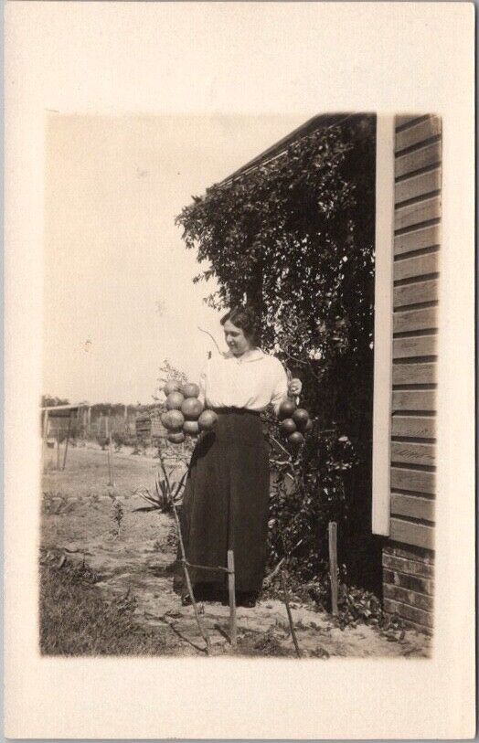 c1910s RPPC Real Photo Postcard Woman Outdoors, Holding Two Bunches of ORANGES
